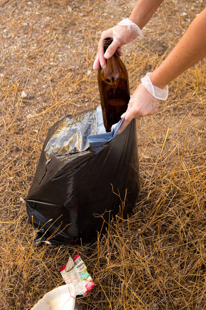 Imagen de las manos de una mujer caucásica recogiendo basura plástica en un prado - Foto, imagen