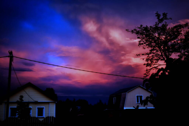 Purpurroter Sonnenuntergang über dem Dorf nach einem Gewitter, Kontrastbild - Foto, Bild