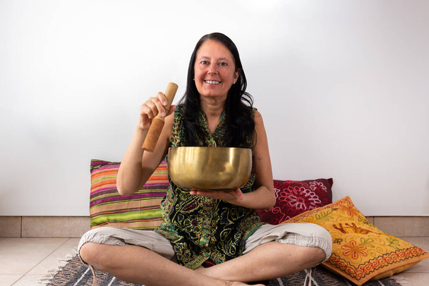 Женщина средних лет с помощью тибетского пения чашу, глядя на камеру с большой улыбкой на лице. - Фото, изображение