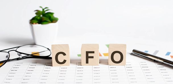 Ahşap bloklara yazılmış CFO sözcük kavramı, çiçekli bir masanın üzerindeki küpler, harita üzerinde kalem ve bardaklar. - Fotoğraf, Görsel