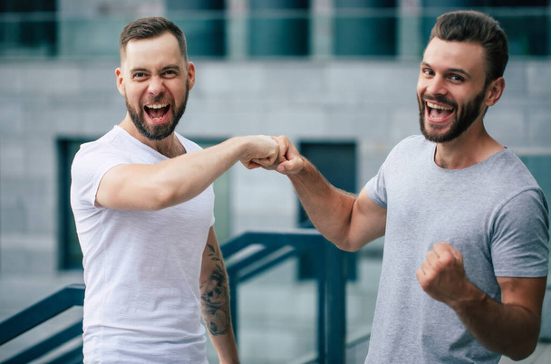 Two happy excited modern bearded best friends in casual clothes having fun and chatting together outdoors. - Foto, imagen