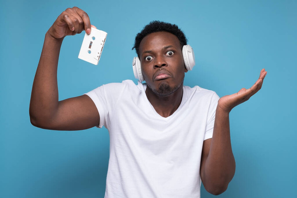 Um jovem afro-americano bonito ouvindo música em fones de ouvido brancos. Desfrute do conceito de música. Estúdio tiro na parede azul. - Foto, Imagem