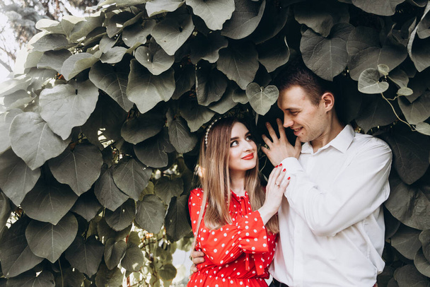 Όμορφο ζευγάρι, ένα κορίτσι με κόκκινο φόρεμα και ένας τύπος με λευκό πουκάμισο, περπατούν στο πάρκο στη φύση - Φωτογραφία, εικόνα