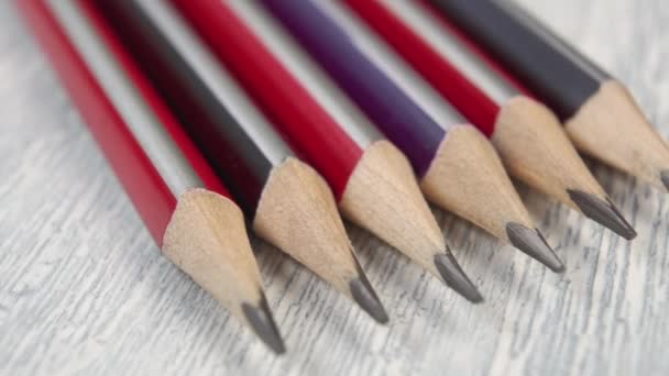 Scherpe grijze potloden in heldere veelkleurige ondergronden. Op een houttextuur. Macro dolly neergeschoten - Video