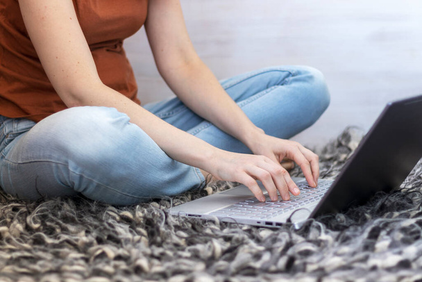 Молодая женщина сидит на ковре ручной работы и работает со своим ноутбуком. - Фото, изображение