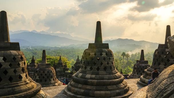 Glorious sunset at Borobudur Temple in East Java, Indonesia. Blue and orange sky over the hills, green jungles and stupa, travel destination, UNESCO World Heritage Site - Photo, Image