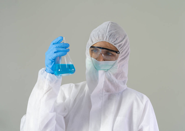 Una scienziata occidentale con tuta e maschera Covid-19 che tiene la provetta per analizzare il vaccino del virus covid-19 in laboratorio o laboratorio in tecnologia medica, chimica, sanità, ricerca scientifica. - Foto, immagini