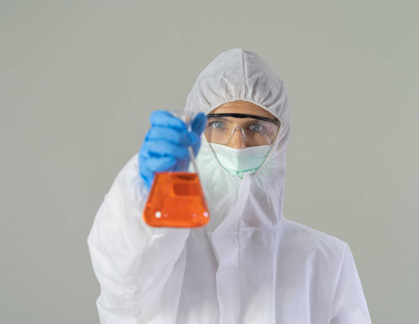 Una mujer científica occidental con traje y máscara Covid-19 que sostiene el tubo de ensayo para analizar la vacuna del virus covid-19 en laboratorio o laboratorio en tecnología médica, química, salud, investigación científica. - Foto, Imagen