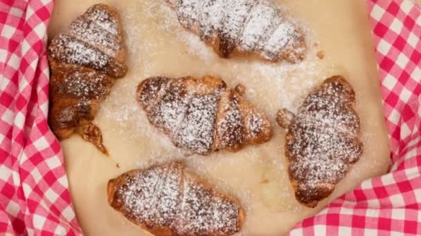 croissant croccanti al forno spruzzati con zucchero a velo su carta pergamena marrone, il cibo ruota, vista dall'alto - Filmati, video