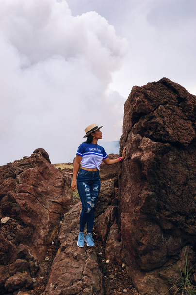 Une femelle portant un chapeau debout sur une énorme roche volcanique à côté du cratère volcanique au parc national du volcan Masaya - Photo, image