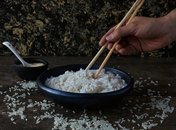 jemand mit Essstäbchen versucht, gekochten Reis mit Samen zu pflücken - Foto, Bild