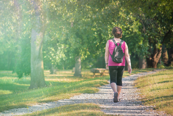 公園を歩いている中年女性、屋外静かな散歩(コピースペース付きの画像) - 写真・画像