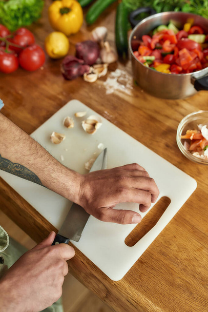 Close up of hands of man, chef cook cutting garlic on the chopping board while preparing a meal in the kitchen - Photo, image