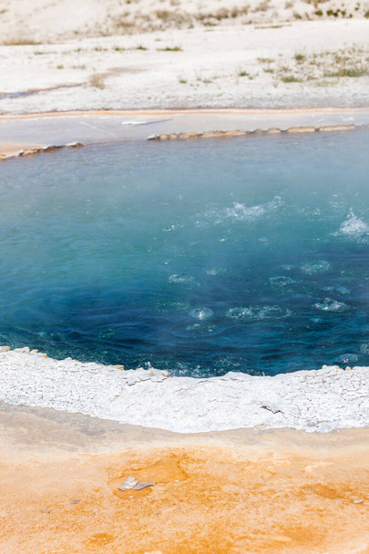 Mélykék forrásban lévő víz a Crested Pool belsejében fehér peremmel a Yellowstone Természeti Parkban. - Fotó, kép