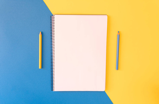 Empty notebook and pencils on yellow and blue background, Top view. Copy space. - Photo, Image