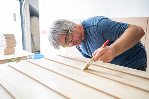 Carpinteiro aplicando verniz para o mobiliário que ele está construindo. - Foto, Imagem
