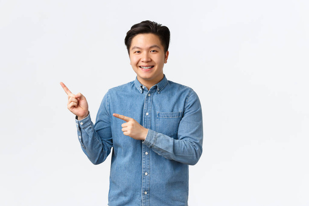 Smiling handsome asian male student showing project, making demonstration or announcement, pointing fingers upper left corner, recommend click link, online courses, white background - Foto, Imagem