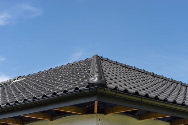 青い空、見える尾根のタイルに対するアントラサイトの新しいセラミックタイルで覆われた一戸建ての屋根. - 写真・画像