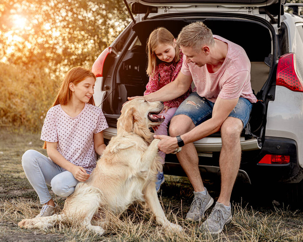 Family with dog next to open car - Фото, изображение