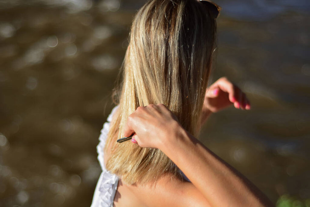 Mulher loira penteia seu cabelo ao ar livre em um dia de verão e fundo borrado com espaço de cópia - Foto, Imagem
