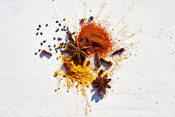 Close-up steranijs, kruidnagel op verschillende poederspecerijen van chili, kurkuma en sesamzaad op een witte achtergrond. - Foto, afbeelding