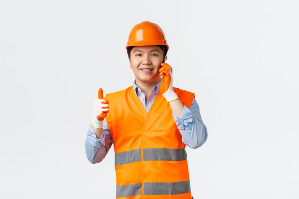 Building sector and industrial workers concept. Construction manager got permission or approval from chief engineer via mobile phone. Architect in helmet show thumbs-up while talking on smartphone - Foto, Imagen