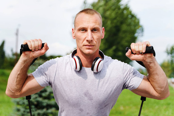 Adult caucasian man training outdoor in summer day - Male athlete using resistance band tubes in his daily workout routine - Real people health and fitness concept - Photo, Image