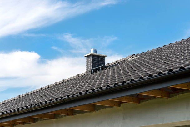 青い空に対するアントラサイトの新しいセラミックタイルで覆われた一戸建ての屋根。タイルで覆われた可視システム煙突. - 写真・画像
