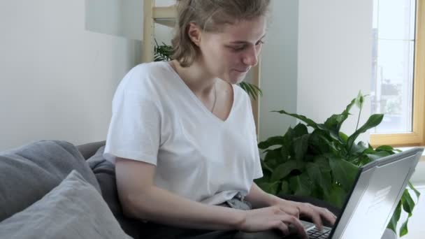усміхнена молода жінка сидить на дивані, використовуючи ноутбук, вводячи повідомлення
 - Кадри, відео