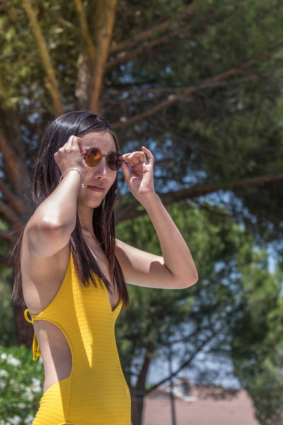 Azjatka w okularach przeciwsłonecznych w żółtym stroju kąpielowym - Zdjęcie, obraz
