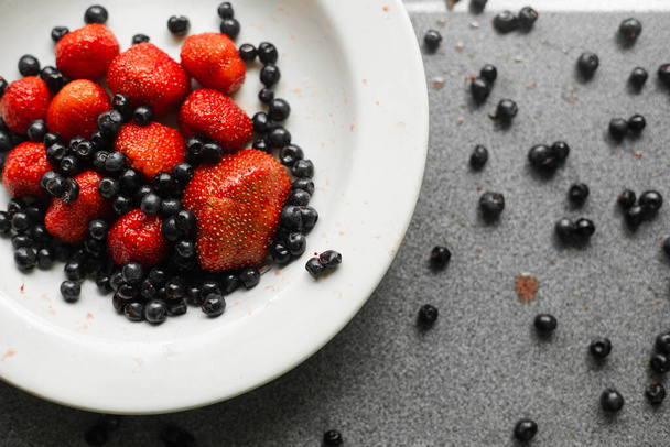 Many juicy fresh ripe red berries and blackberries lie in a white ceramic plate on the table - Photo, Image