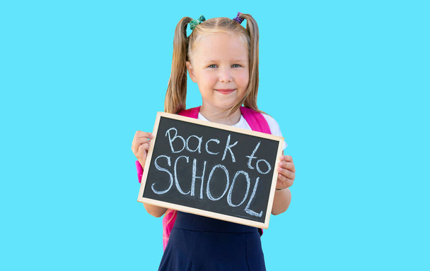 schoolgirl holds a sign with the words "Back to school" in her hands. isolate on blue background - Фото, изображение