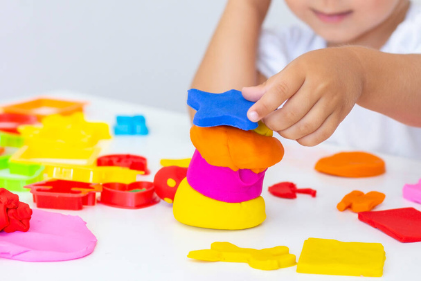 Toddler sculpts from colored plasticine on a white table. The hand of a small child squeezes pieces of colored plasticine. Childrens creativity, educational games, fine motor skills - Foto, Bild