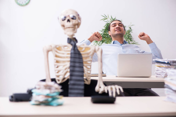 Giovane dipendente maschio e scheletro in ufficio - Foto, immagini