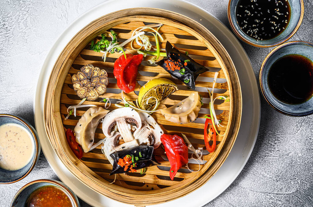 Geleneksel bambu buharlı tencerede ev yapımı Çin yemeği ve Kore böreği servis ediliyor. Gri arka plan. Üst görünüm. - Fotoğraf, Görsel