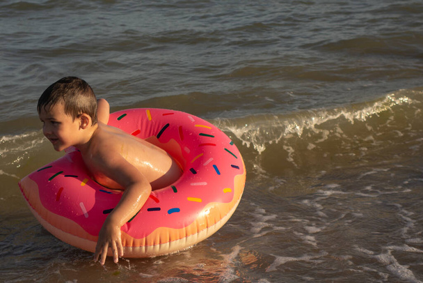 niño de 5 años se baña en el mar en un anillo de vida en un día soleado - Foto, Imagen