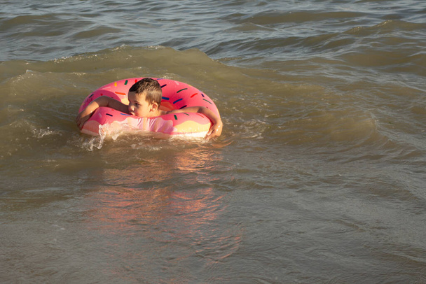5-річний хлопчик купається в морі в рятувальному кільці на сонячний день
 - Фото, зображення