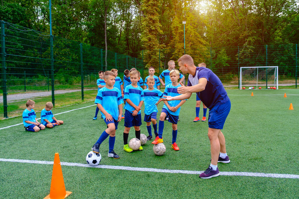 Kinderen in voetbaluniform luisteren naar uitleg over coach op training. Jonge coach legt voetbal spel strategie uit aan kinderen voetbalteam.  - Foto, afbeelding