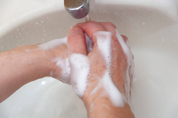 Πλένει τα χέρια με σαπούνι και νερό για προστασία από τον ιό Coronavirus COVID-19 και άλλες μεταδοτικές ασθένειες. Κοντινό πλάνο. Στο πάνω μέρος. Οριζόντια βολή. - Φωτογραφία, εικόνα