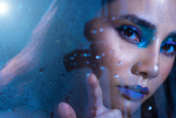 Portrait of Fashion 20s Asian Woman has beautiful update make up artist, she apply Fashionable eyes cosmetic, sexy feeling poses over Blue Tone Bathroom steam on glass - 写真・画像