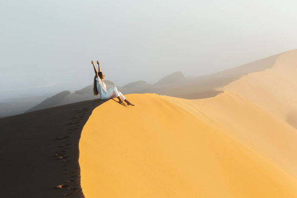 Мечта, путешествия и концепция. Счастливая женщина, вдохновленная фантастическим восходом солнца в пустынных песчаных дюнах Сахары, Марокко. Туман утром и теплый свет. - Фото, изображение
