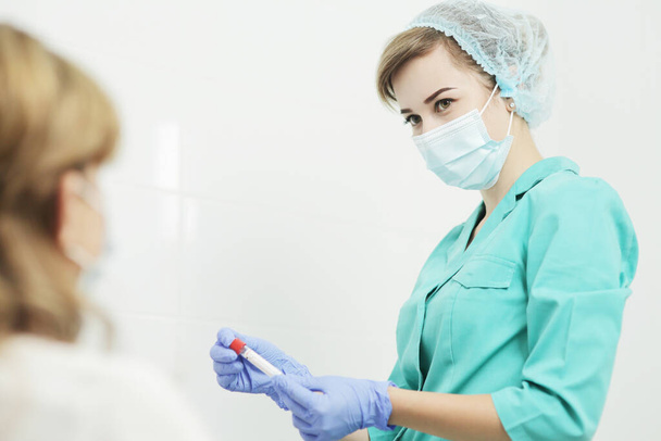 Tıbbi maskeli kadın hemşire kan testi için tüp tutuyor. - Fotoğraf, Görsel