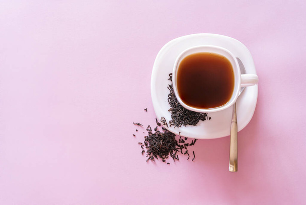Ένα φλιτζάνι τσάι με φύλλα τσαγιού σε ροζ φόντο, κορυφαία άποψη. - Φωτογραφία, εικόνα