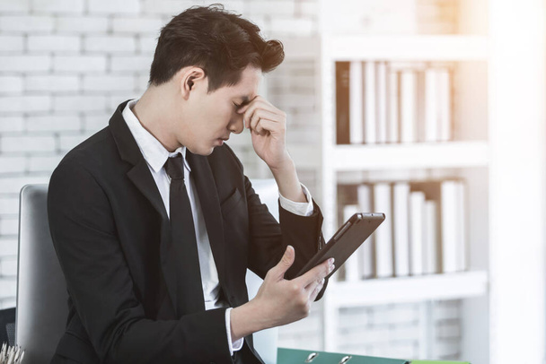 Stressed businessman worked with a tablet and having a headache after business losses In the office room background. - 写真・画像