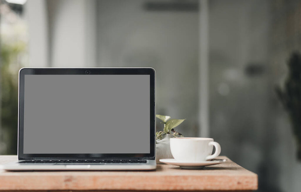 Mockup of laptop computer with empty screen with coffee cup on table of the coffee shop background,gray screen - Фото, зображення
