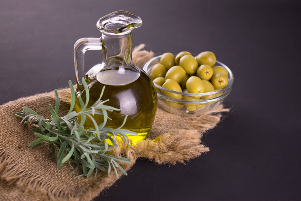 Olive oil in a bottle and fresh rosemary on a dark background. - Photo, Image