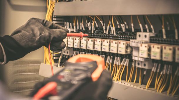 Ingeniero eléctrico que utiliza equipos de medición digitales de varios medidores para verificar el voltaje de corriente eléctrica en el disyuntor y el sistema de cableado de cable en la placa de distribución de energía principal. - Foto, imagen