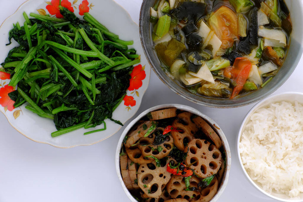 Top view comida diaria vegana para el almuerzo, la raíz de loto en rodajas cocinero con salsa, sopa de verduras, tazón de arroz, espinacas fritas, comida vietnamita vegetariana simple para la dieta, pero bueno para la salud - Foto, imagen