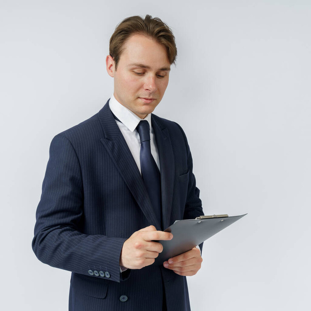 Biznesmen w niebieskim garniturze trzyma teczkę w rękach i czyta raporty na białym tle. Koncepcja biznesowa i finansowa - Zdjęcie, obraz