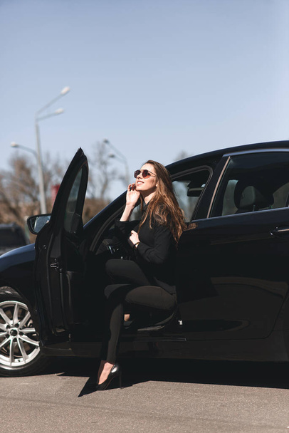 Joven mujer de negocios en desgaste negro con coche caro - Foto, imagen